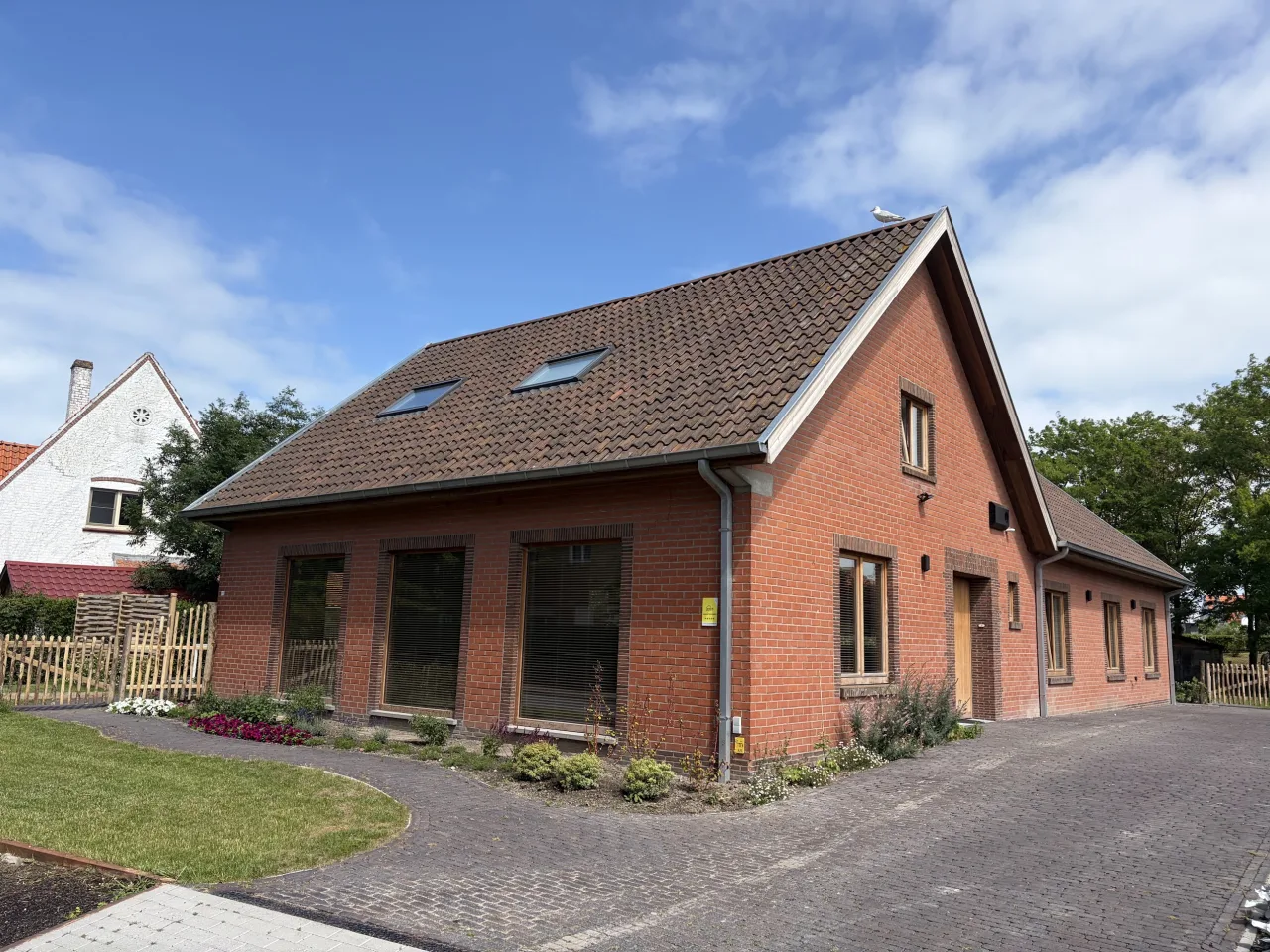 De voorgevel van Kia Ora in de zomer, met bloeiende borders langs de geplaveide oprit.